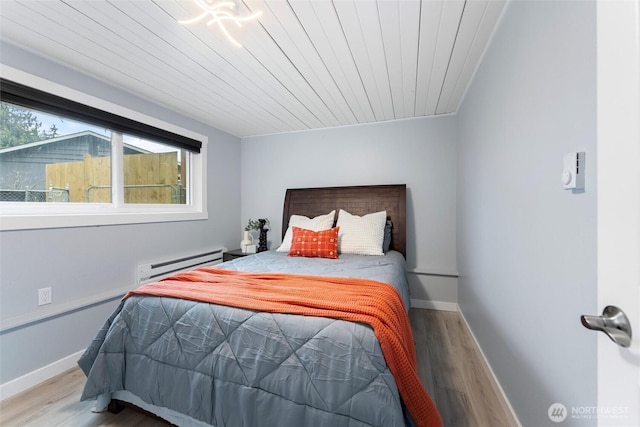 bedroom with a baseboard heating unit, wooden ceiling, baseboards, and wood finished floors