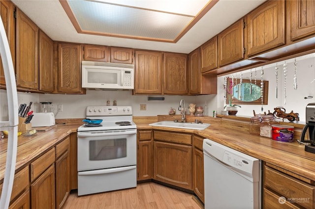 kitchen with sink, white appliances, light hardwood / wood-style flooring, wooden counters, and a tray ceiling