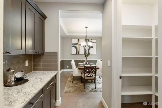 interior space with dark brown cabinetry, a tray ceiling, light stone countertops, light hardwood / wood-style floors, and backsplash