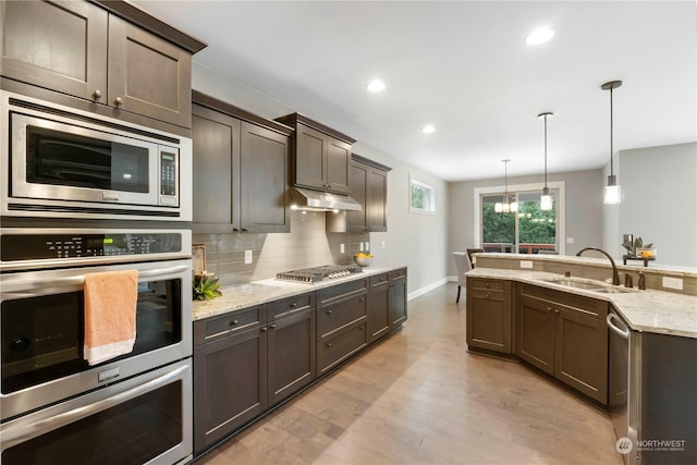 kitchen with sink, hanging light fixtures, stainless steel appliances, dark brown cabinetry, and decorative backsplash