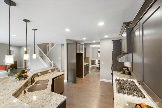 kitchen with pendant lighting, dishwasher, sink, light stone countertops, and dark wood-type flooring