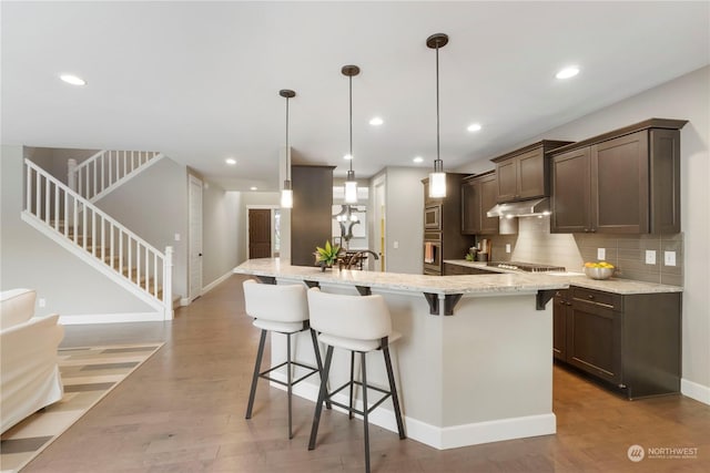 kitchen featuring pendant lighting, a breakfast bar area, light stone counters, stainless steel appliances, and a spacious island