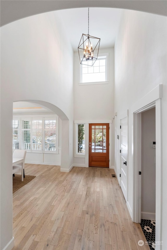 foyer entrance with a high ceiling, a notable chandelier, and light wood-type flooring