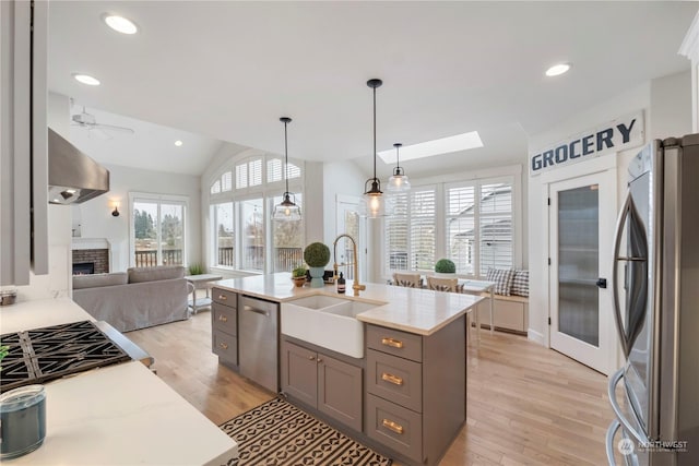 kitchen with pendant lighting, sink, appliances with stainless steel finishes, light hardwood / wood-style floors, and a center island with sink