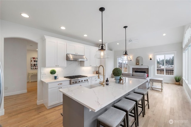 kitchen with decorative light fixtures, sink, white cabinets, a kitchen island with sink, and stainless steel gas cooktop