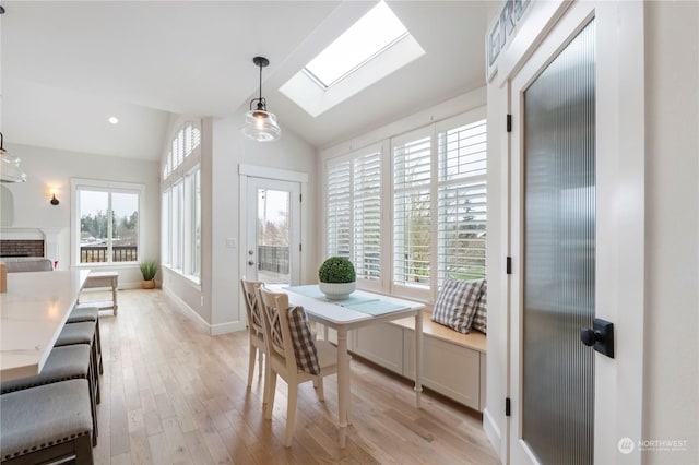 dining area featuring a fireplace, light hardwood / wood-style floors, and vaulted ceiling with skylight