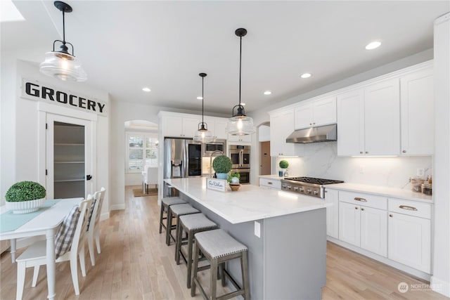 kitchen featuring hanging light fixtures, stainless steel appliances, white cabinets, a kitchen island, and decorative backsplash