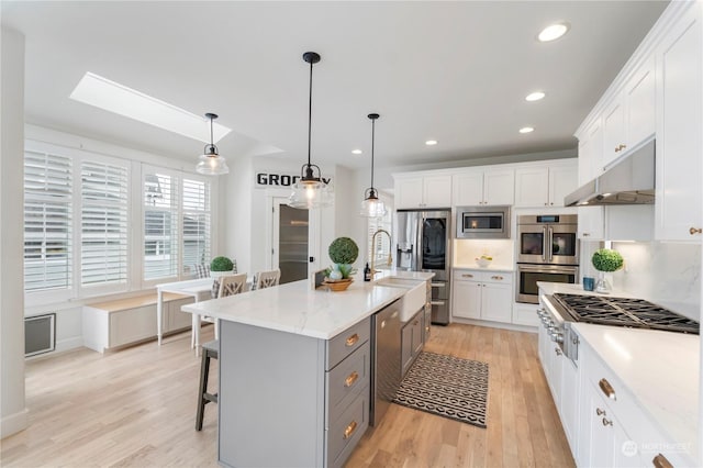 kitchen with pendant lighting, an island with sink, white cabinets, and appliances with stainless steel finishes