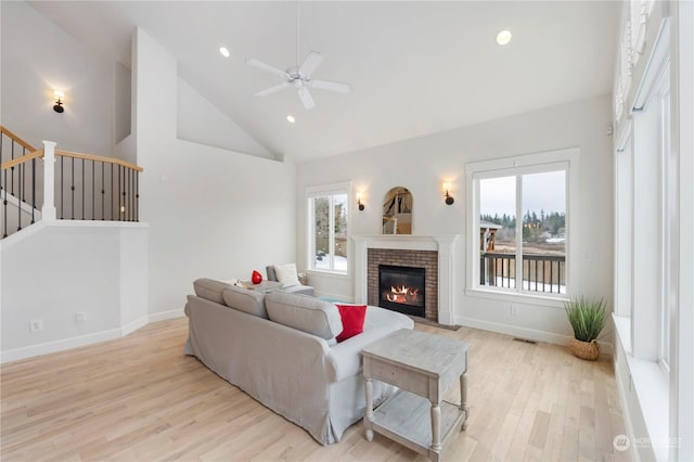 living room with high vaulted ceiling, light hardwood / wood-style floors, a healthy amount of sunlight, and a brick fireplace