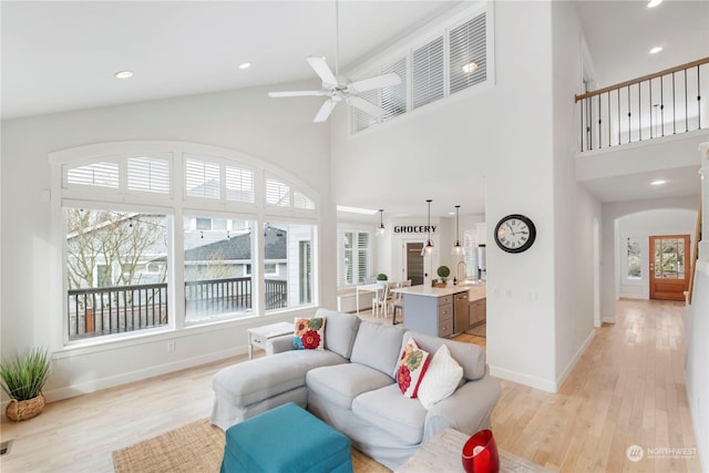 living room featuring ceiling fan, a towering ceiling, and light hardwood / wood-style floors