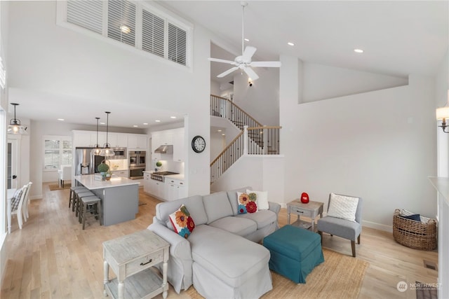 living room with light hardwood / wood-style floors, ceiling fan, and a high ceiling