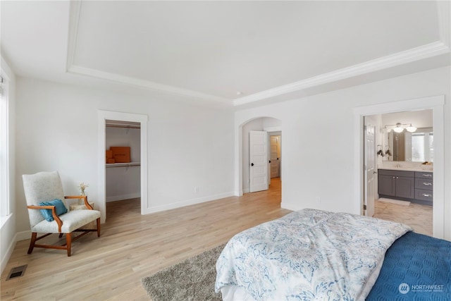 bedroom featuring a spacious closet, light hardwood / wood-style flooring, a raised ceiling, and ensuite bathroom