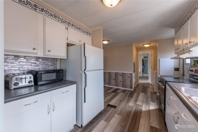 kitchen with white cabinetry, white refrigerator, stainless steel range with electric cooktop, and hardwood / wood-style flooring