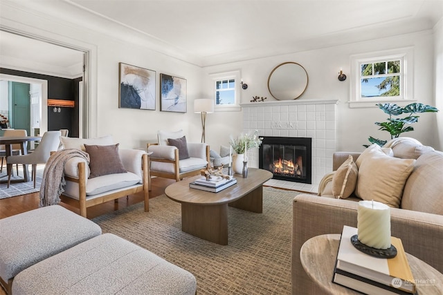 living room with ornamental molding, a wealth of natural light, a tile fireplace, and wood-type flooring