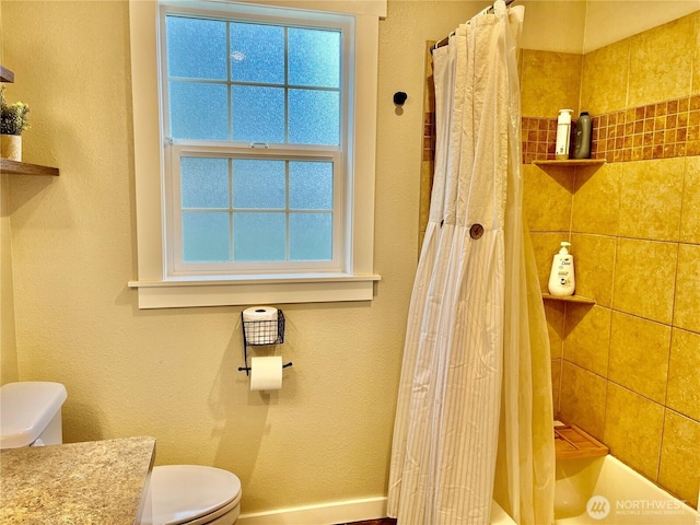 bathroom with a textured wall, shower / bathtub combination with curtain, toilet, vanity, and baseboards