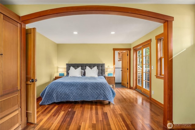 bedroom with baseboards, arched walkways, wood finished floors, and access to exterior