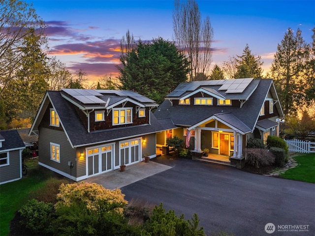 view of front of property featuring a shingled roof, roof mounted solar panels, fence, and driveway