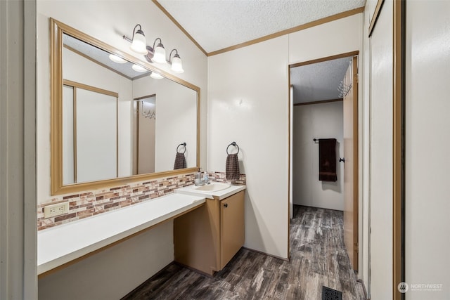 bathroom with a textured ceiling, ornamental molding, vanity, hardwood / wood-style flooring, and backsplash