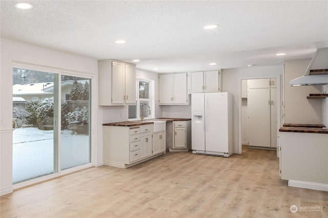 kitchen with sink, white cabinetry, a textured ceiling, white fridge with ice dispenser, and light hardwood / wood-style floors