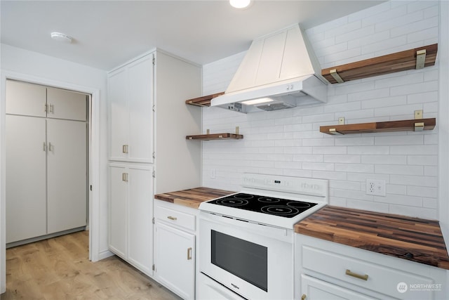 kitchen with butcher block counters, custom exhaust hood, white range with electric cooktop, decorative backsplash, and white cabinets