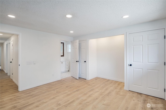 unfurnished bedroom featuring connected bathroom, a textured ceiling, and light wood-type flooring