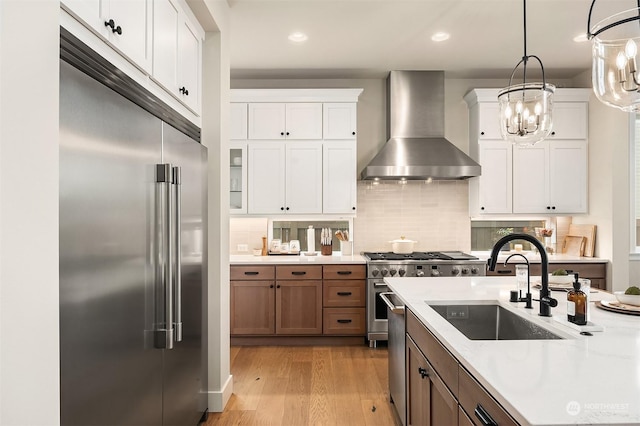 kitchen featuring wall chimney exhaust hood, white cabinetry, high quality appliances, and light stone counters