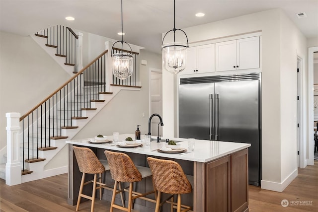 kitchen with dark wood-type flooring, a kitchen island with sink, white cabinets, decorative light fixtures, and built in fridge