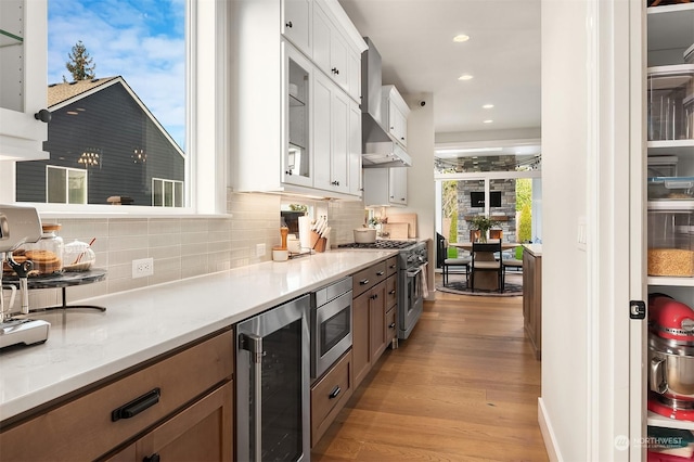 kitchen with appliances with stainless steel finishes, tasteful backsplash, white cabinets, beverage cooler, and wall chimney exhaust hood