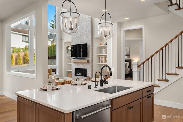 kitchen with sink, stainless steel dishwasher, pendant lighting, a fireplace, and a kitchen island with sink