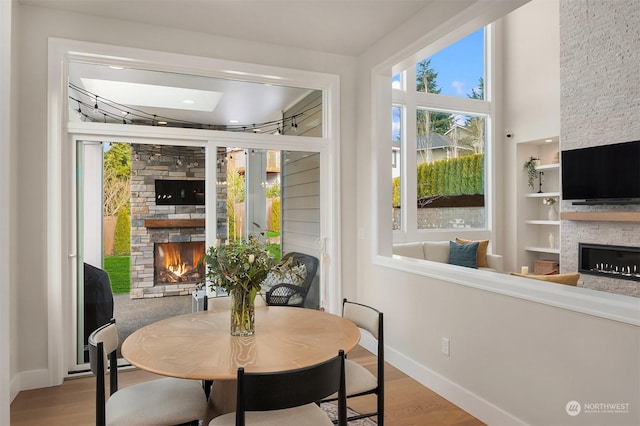 dining area featuring a stone fireplace, built in shelves, and light wood-type flooring