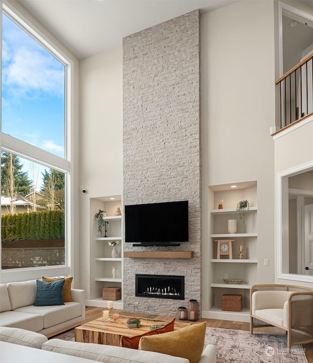 living room with hardwood / wood-style flooring, a stone fireplace, built in features, and a high ceiling