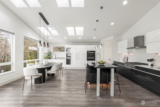 kitchen featuring stainless steel gas cooktop, white cabinetry, hanging light fixtures, an island with sink, and wall chimney range hood