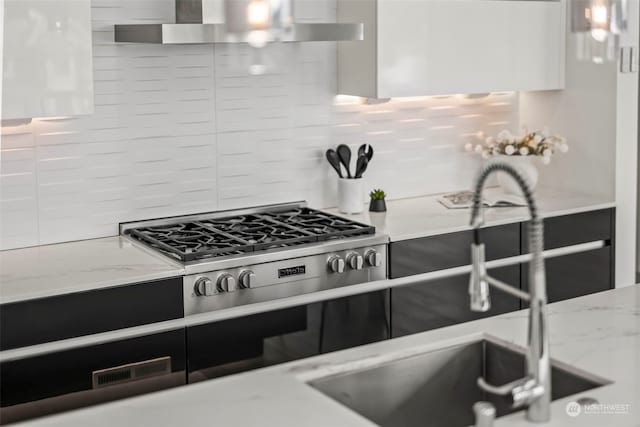 kitchen featuring sink, wall chimney range hood, light stone countertops, stainless steel gas cooktop, and decorative backsplash