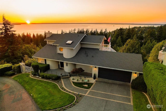 view of front of house featuring a garage, a water view, and a lawn