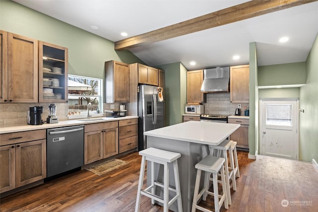 kitchen with sink, stainless steel appliances, a center island, a kitchen bar, and wall chimney exhaust hood