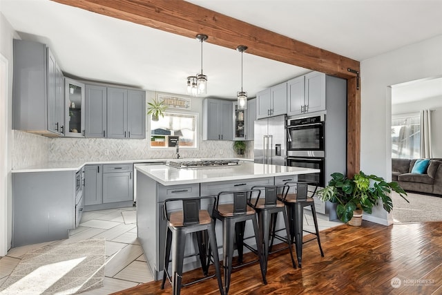 kitchen featuring backsplash, beam ceiling, stainless steel appliances, a center island, and a kitchen breakfast bar