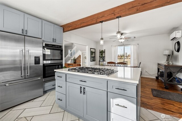 kitchen with gray cabinets, ceiling fan, a wall unit AC, stainless steel appliances, and beamed ceiling