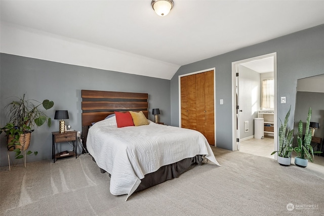 bedroom featuring light colored carpet, lofted ceiling, and ensuite bathroom