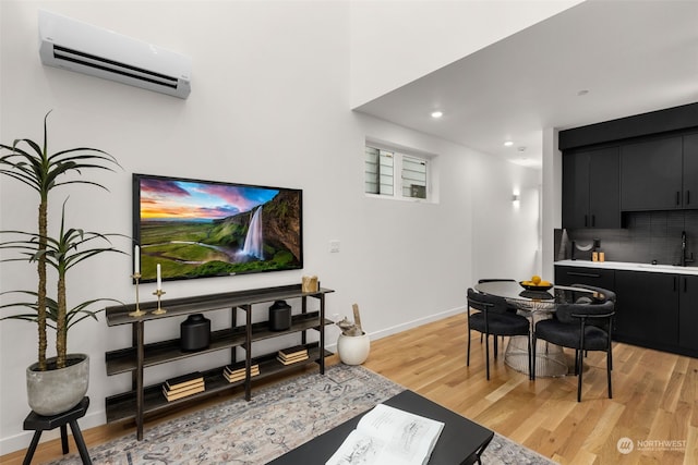 living room with sink, a wall unit AC, and light hardwood / wood-style floors