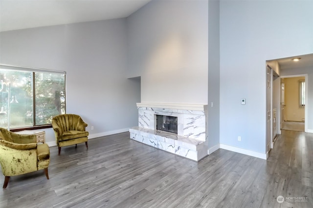 unfurnished living room featuring high vaulted ceiling, a premium fireplace, wood finished floors, and baseboards