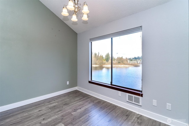 empty room with vaulted ceiling, hardwood / wood-style floors, a notable chandelier, a water view, and a textured ceiling