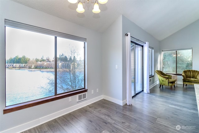 interior space featuring an inviting chandelier, vaulted ceiling, hardwood / wood-style floors, and a textured ceiling