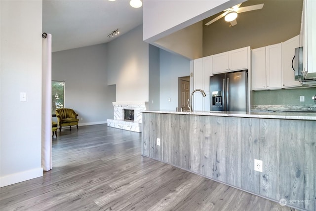 kitchen with refrigerator with ice dispenser, white cabinets, a fireplace with raised hearth, stainless steel microwave, and high vaulted ceiling