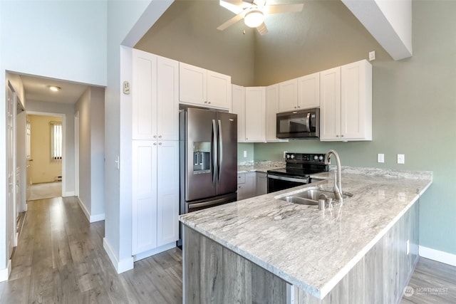 kitchen featuring baseboards, appliances with stainless steel finishes, light stone counters, a peninsula, and a sink