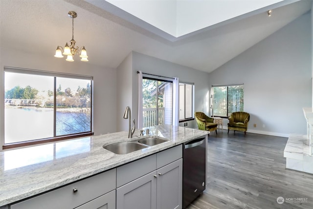 kitchen with light stone counters, pendant lighting, lofted ceiling, a sink, and dishwasher