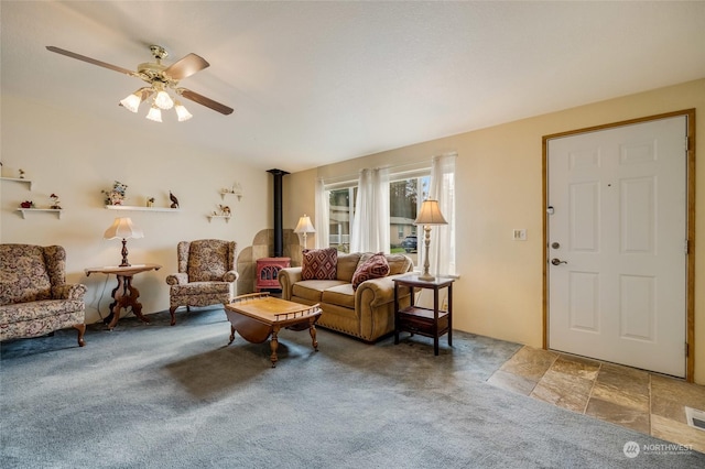 living room featuring carpet flooring, ceiling fan, and a wood stove