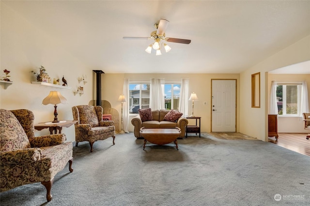 carpeted living room featuring ceiling fan, a healthy amount of sunlight, vaulted ceiling, and a wood stove