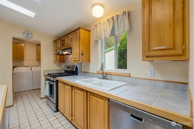 kitchen with appliances with stainless steel finishes, sink, tile counters, light tile patterned floors, and washer and clothes dryer