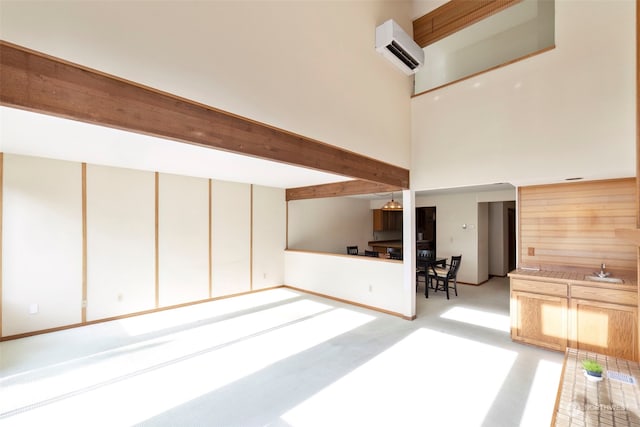 unfurnished living room with beamed ceiling, an AC wall unit, a high ceiling, and sink