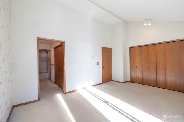 unfurnished bedroom featuring a closet, ensuite bathroom, high vaulted ceiling, and light carpet